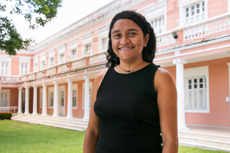 Imagem: Foto da estudante Laianne Plácido Lima vestindo uma blusa na cor preta nos jardins da Reitoria
