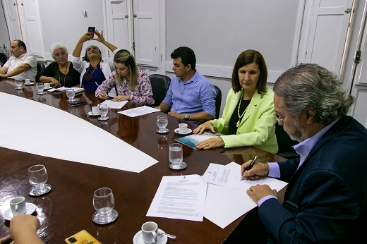 Imagem: Várias pessoas sentadas em torno de uma mesa, no momento da assinatura do protocolo de intenções (Foto: Viktor Braga/UFC)