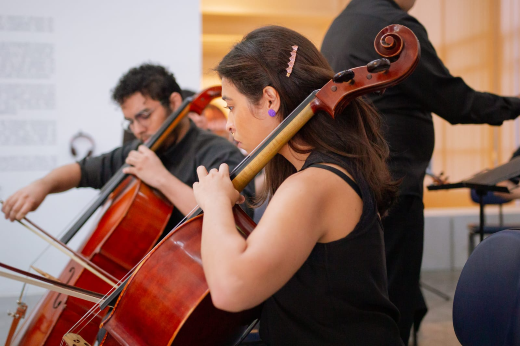 Imagem: Foto aproximada de dois violoncelistas executando um concerto
