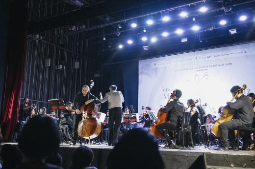 Imagem: Foto do palco do Teatro da Tapera das Artes com um solista de contrabaixo acústico, o maestro e a orquestra de cordas