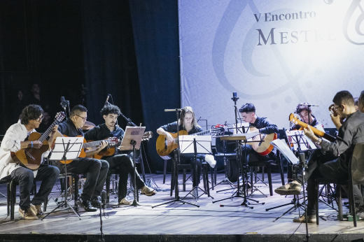Imagem: Foto da Orquestra de violões do V Encontro Mestre e Aprendiz com os músicos sentados em um formato de meia-lua