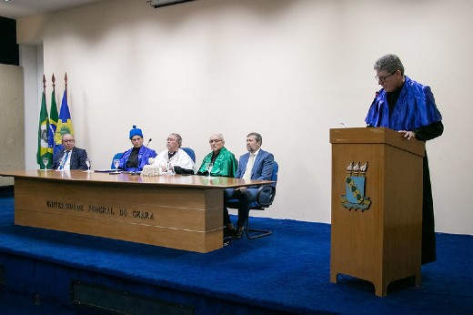 Imagem: Foto do pró-reitor Augusto Albuquerque discursando no púlpito, e, ao fundo, a mesa solene do evento