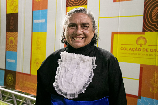 Imagem: uma senhora de cabelos grisalhos vestida de beca sorri para a foto