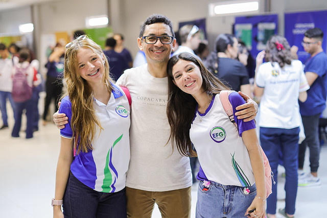 Fotografia do Professor Renato com duas de suas estudantes em visita à Feira das Profissões da UFC (Foto: Ribamar Neto/UFC)