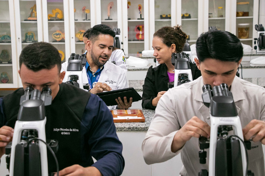Imagem: pessoas, em primeiro plano, olhando no microscópio em ambiente de laboratório