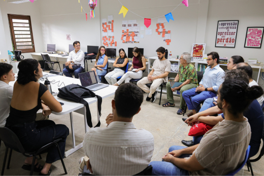 Imagem: Foto de pessoas sentadas em semicírculo na sala de reunião do IAUD