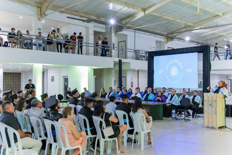 Imagem: Colação de grau da UFC em Crateús, realizada em um espaço interno. Formandos, familiares e professores acompanham a cerimônia, marcada pela solenidade e celebração da conclusão da graduação.