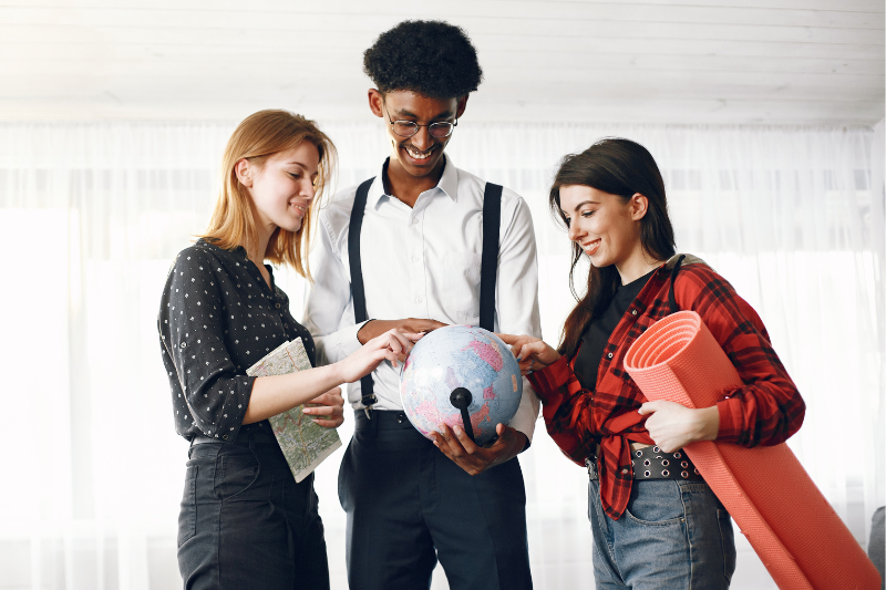 Programa UFC Mundo - Ações Afirmativas seleciona alunos para intercâmbio nas universidades de Frankfurt e Salento (Imagem: Freepik) Imagem: Foto de um rapaz negro e duas moças brancas segurando um globo terrestre, enquanto uma delas apoia um mapa múndi e a outra, um tapete EVA vermelho enrolado
