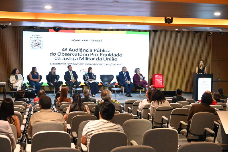 Imagem: Grupo de pessoas em auditório sentadas e olhando para mesa de debatedores da audiência 