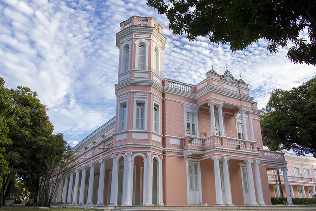 Fachada de um prédio rosa. Ao fundo, um céu com muitas nuvens