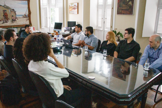 Imagem: Foto dos participantes do SteelChallenge sentados na mesa de reunião do Gabinete da Reitoria