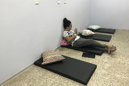 Imagem: foto de uma jovem sentada em um dos colchonetes pretos que estão no chão da sala