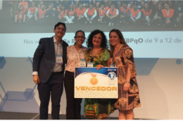 Imagem: foto de quatro pessoas em um palco sorrindo para a foto e segurando um cartaz com prêmio