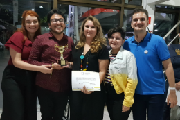 Imagem: foto de pessoas sorrindo e segurando um troféu e um certificado