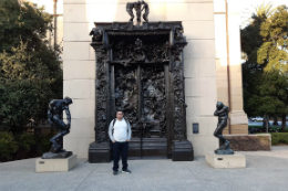 Imagem: foto de Diego Cavalcante em frente a uma grande porta com estátuas nas laterais