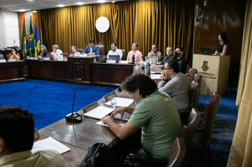 Imagem: reunião na sala do Consuni com pessoas sentadas à mesa e uma pessoa falando no púlpito. (Ribamar Neto) 