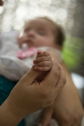 Imagem: foto de mãe segurando mão de um bebê e, ao fundo, rosto do bebê desfocado