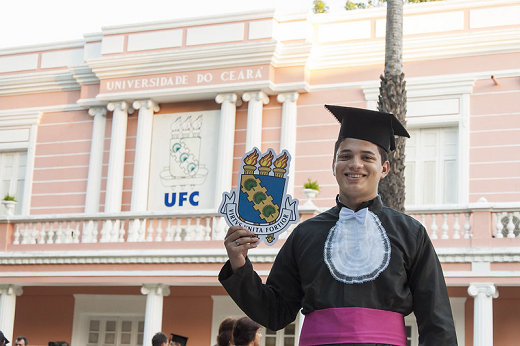 Imagem: estudante com beca em frente à Reitoria