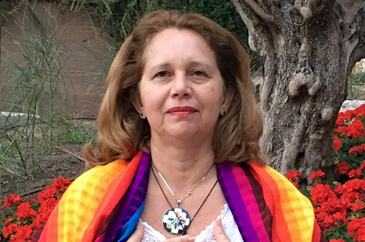 Foto da Profª Germana Moraes. Ela usa uma camisa branca e um xale colorido