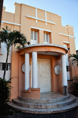 Imagem: Foto da fachada do Teatro Universitário, prédio em tons claros, com entrada arredondada, com quatro pequenas colunas sob a marquise (Foto: Ribamar Neto/UFC) 