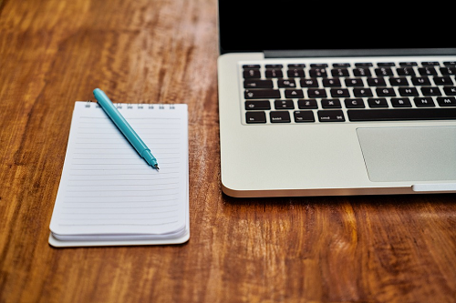 Imagem: foto de um notebook em uma mesa ao lado de bloco de notas