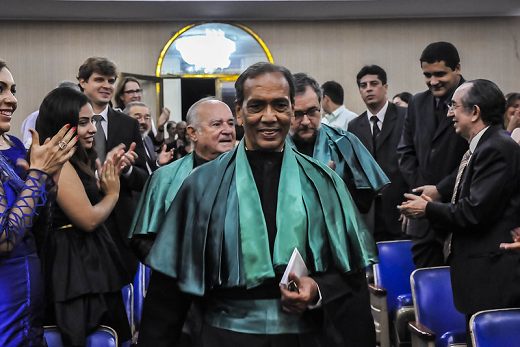 Prof. Vietla vestido com trajes especiais para receber o título de professor emérito da UFC. Pessoas ao redor dele batem palmas