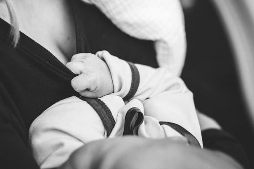 Foto em P&B de bebê agarrando o peito da mãe para mamar