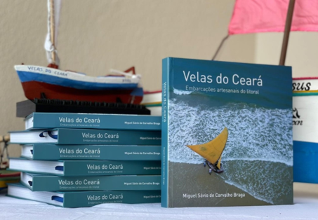 Imagem: foto com livros empilhados e ao lado um de pé, onde se vê capa com foto de uma jangada na praia