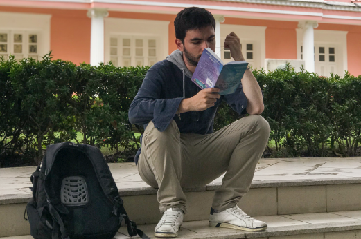 Imagem: estudante sentado em escada da Reitoria lendo um livro