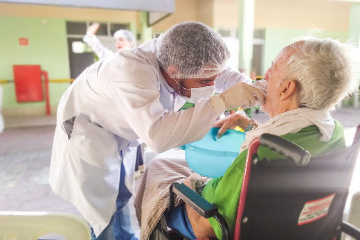 Imagem: estudante de Odontologia examina boca de idoso sentado em cadeira de rodas em abrigo
