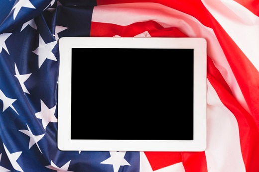 Imagem: foto da bandeira dos Estados Unidos amassada e um tablet em cima