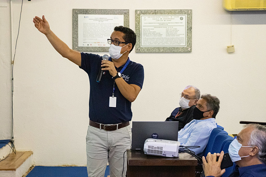 Imagem: foto de um homem de blusa azul segurando o microfone com uma mão e o outro braço levantado