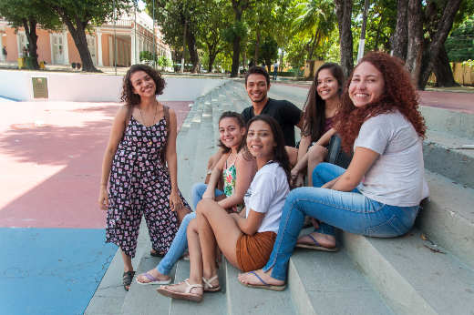 Imagem: foto de estudantes, hommens e mulheres, sentados nos degraus da concha acústica, sem máscaras, antes da pandemia