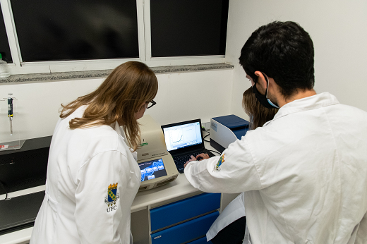 Imagem: Pesquisadores olhando para notebook na bancada do laboratório