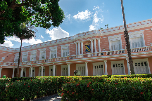 Imagem: Vista lateral da Reitoria da UFC mostra o brasão da Universidade, com o jardim em primeiro plano. (Foto: Viktor Braga)