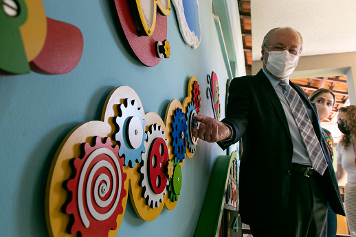 Imagem mostra reitor Cândido Albuquerque movimentando engrenagens coloridas, presas a uma parede, que são utilizadas no desenvolvimento de habilidades nos autistas