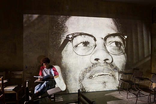 Imagem: Na cena, o estudante Saulo (Lucas Limeira) e, em destaque, imagem de Malcolm X (1925-1965), um dos mais importantes líderes do movimento antirracista afro-americano (Foto: Marcos Hirano)