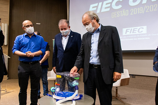 Imagem: ao redor de uma mesa onde está o capacete elmo, aparecem, da esquerda para a direita, o diretor da ESP, Marcelo Alcântara; o presidente da FIEC, Ricardo Cavalcante; e o reitor da UFC, Cândido Albuquerque