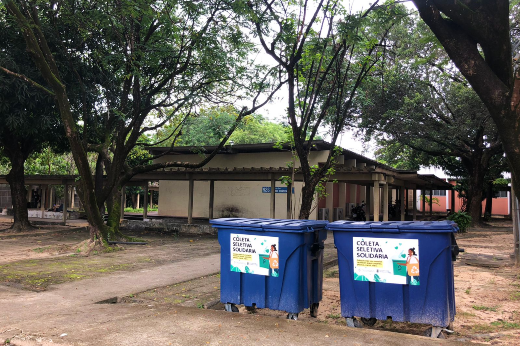 Imagem: Imagem mostra, em primeiro plano, dois depósitos de reciclagem. Ao fundo, um imóvel de tons claros e muitas árvores (Foto: UFC Informa)