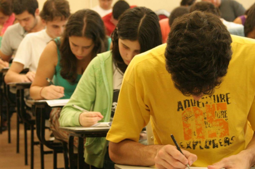 Imagem: estudantes sentados em carteira em sala de aula fazendo prova