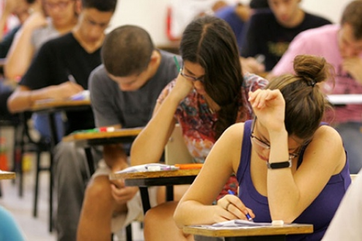 Imagem: estudantes de cabeça baixa fazendo prova em sala de aula
