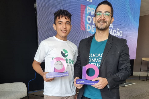 Foto de dois jovens em um palco, cada um segura um troféu