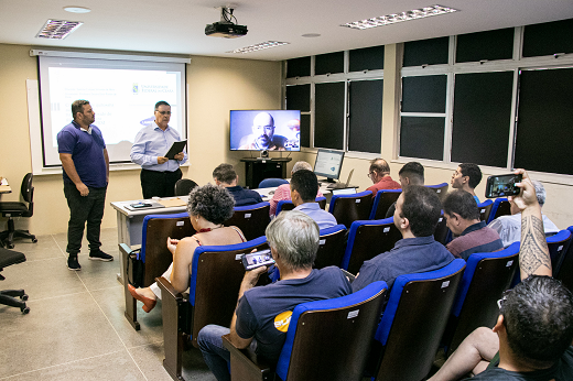 Imagem: Foto mostra o autor, Santino Loruan (de azul, à esquerda), ao lado do orientador, Prof. Enio Ponte, apresentando o projeto de tese diante do público. (Foto: Ribamar Neto/ UFC informa)