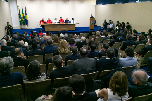 Imagem: Imagem: ambiente de auditório com público sentado e a mesa formada ao fundo com autoridades