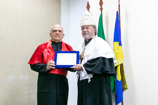 Imagem: homens de vestido preto um com capa vermelha e outra com capa branca que entrega diploma 