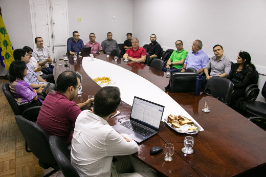 Imagem: sala de reuniões com mesa de madeira e pessoas sentadas ao redor