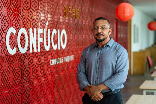 Imagem: Professor Nonato Furtado posa em frente a parede vermelha onde a palavra Confúcio está escrita com letras brancas (Foto: Viktor Braga/UFC Informa) 