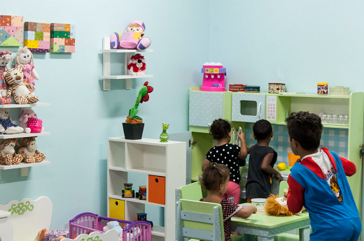 Foto da brinquedoteca da UFC com duas meninas e um menino de costas brincando numa cozinha de brinquedo