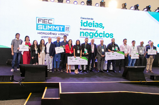 Imagem: pessoas em pé em um palco segurando certificados de premiação