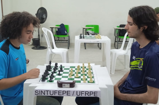Imagem: dois rapazes sentados em mesa disputando uma partida de xadrez